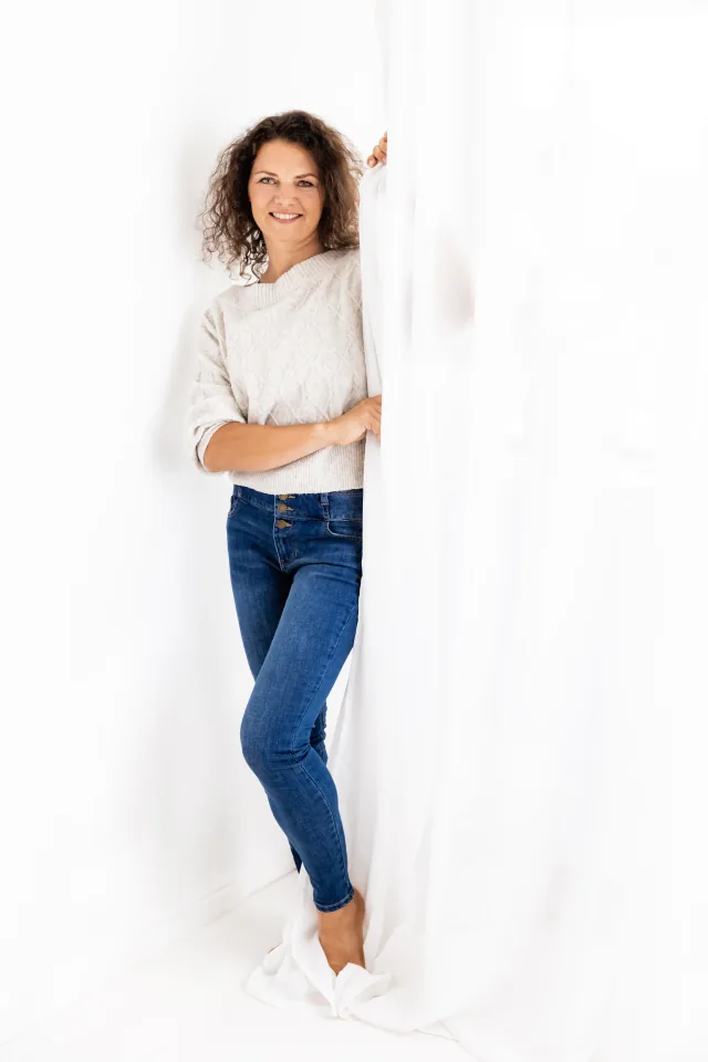 Tanja Želj Zupančič v svetlem puloverju ob beli zavesi